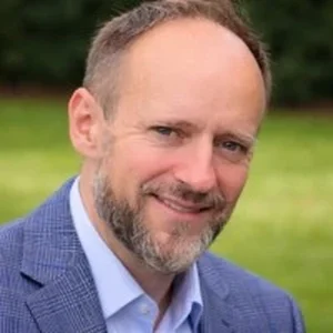 Alexanderhazelldataprotectionconsultant westbrook data protection services limited Smiling man in a blue blazer and light blue shirt outdoors with a green field in the background.